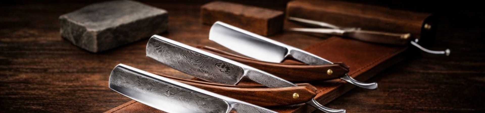 Hand-forged straight razor collection featuring pattern-welded Damascus steel and mirror-polished high-carbon stainless steel blades with wooden scales on a leather strop for wholesale